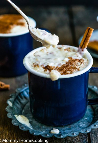 a spoon scooping arroz con leche from a blue cup over a metal plate.