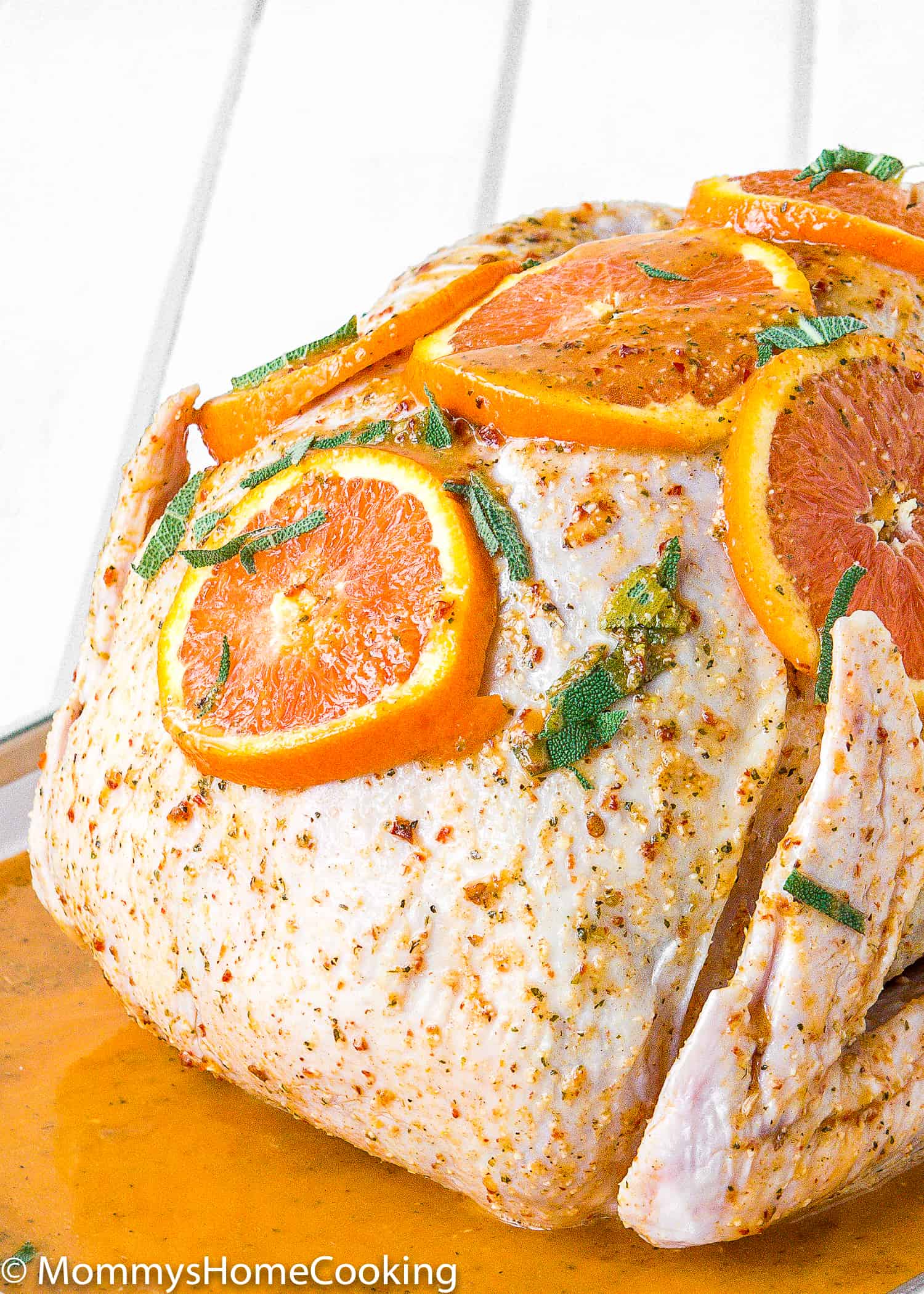close up view of a raw turkey with citrus chipotle marinade with orange slices and herbs on top.