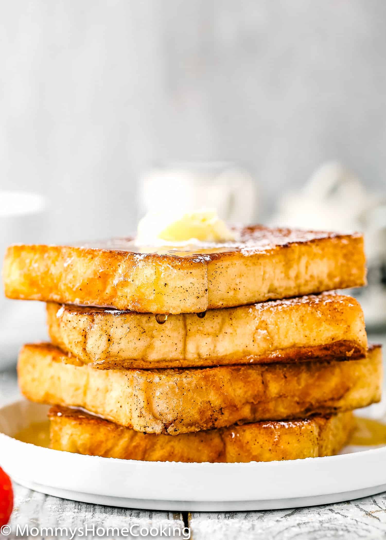A stack of four eggless French toast in a plate with powdered sugar dusted on top and maple syrup.