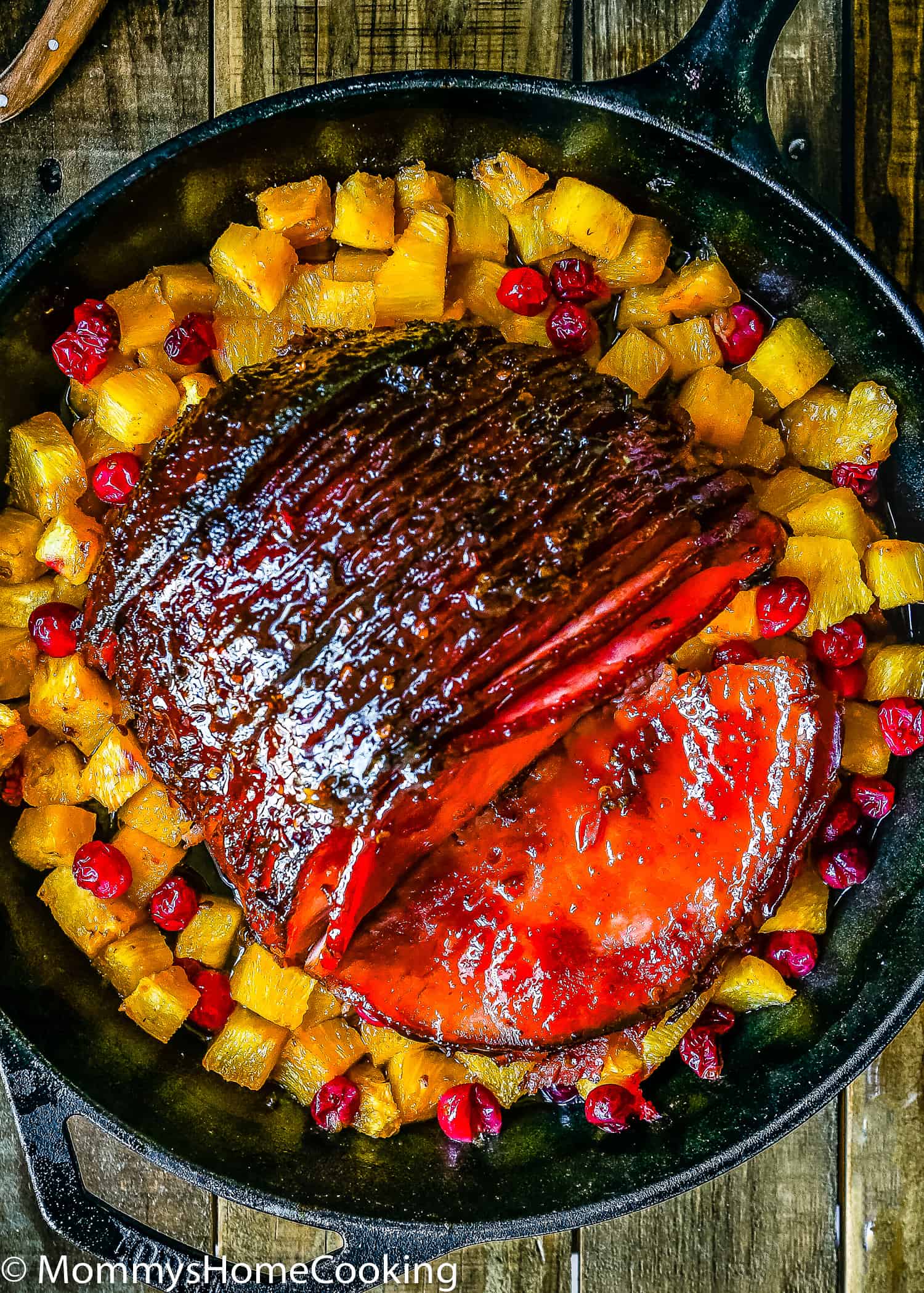 a sliced chipotle glazed ham in a cash iron skillet with pineapple and cranberries.