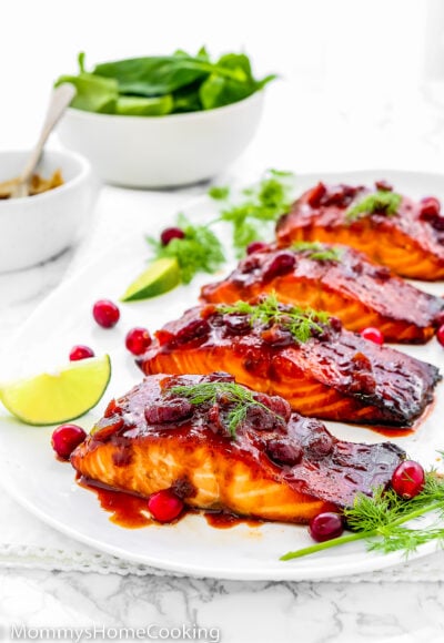 Cranberry Honey Glazed Salmon in a serving plate with fresh cranberries, lemon slices and dill over a marble surface.