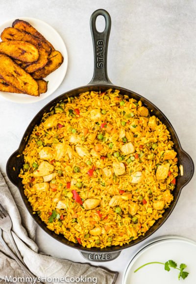 a cast iron skillet with arroz con pollo and a plate of fried plantains on the side.
