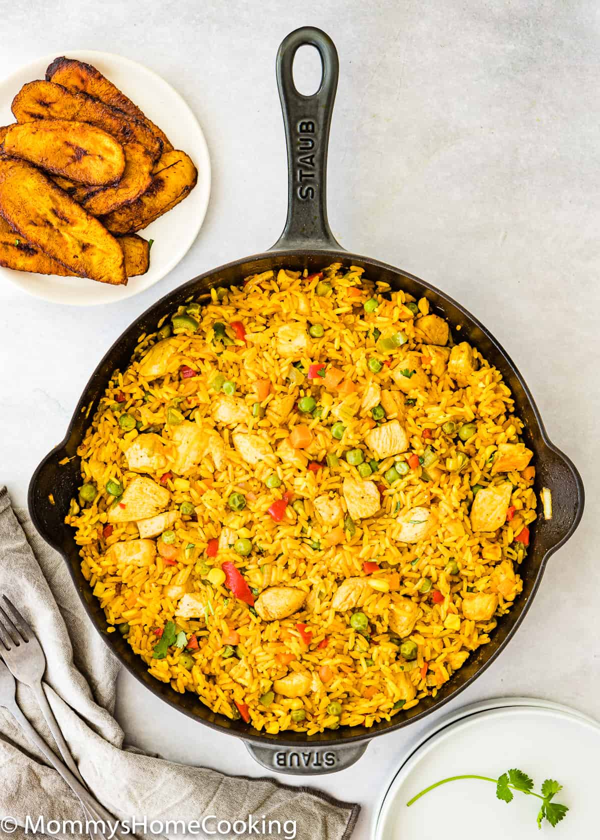 a cast iron skillet with arroz con pollo and a plate of fried plantains on the side.