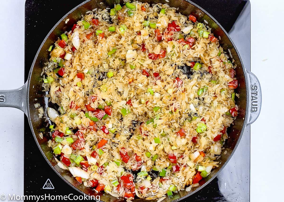 un cooked rice and veggies being sautéed in a skillet.