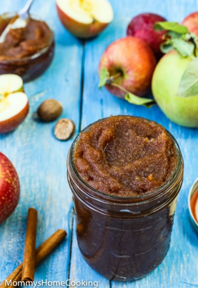 apple butter in a mason jar with fresh apples and cinnamon on the sides