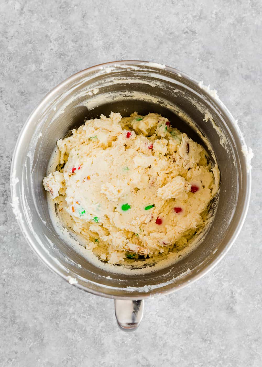 egg-free cookie dough in a stand mixer bowl with m&ms, white chocolate chips and pretzels.