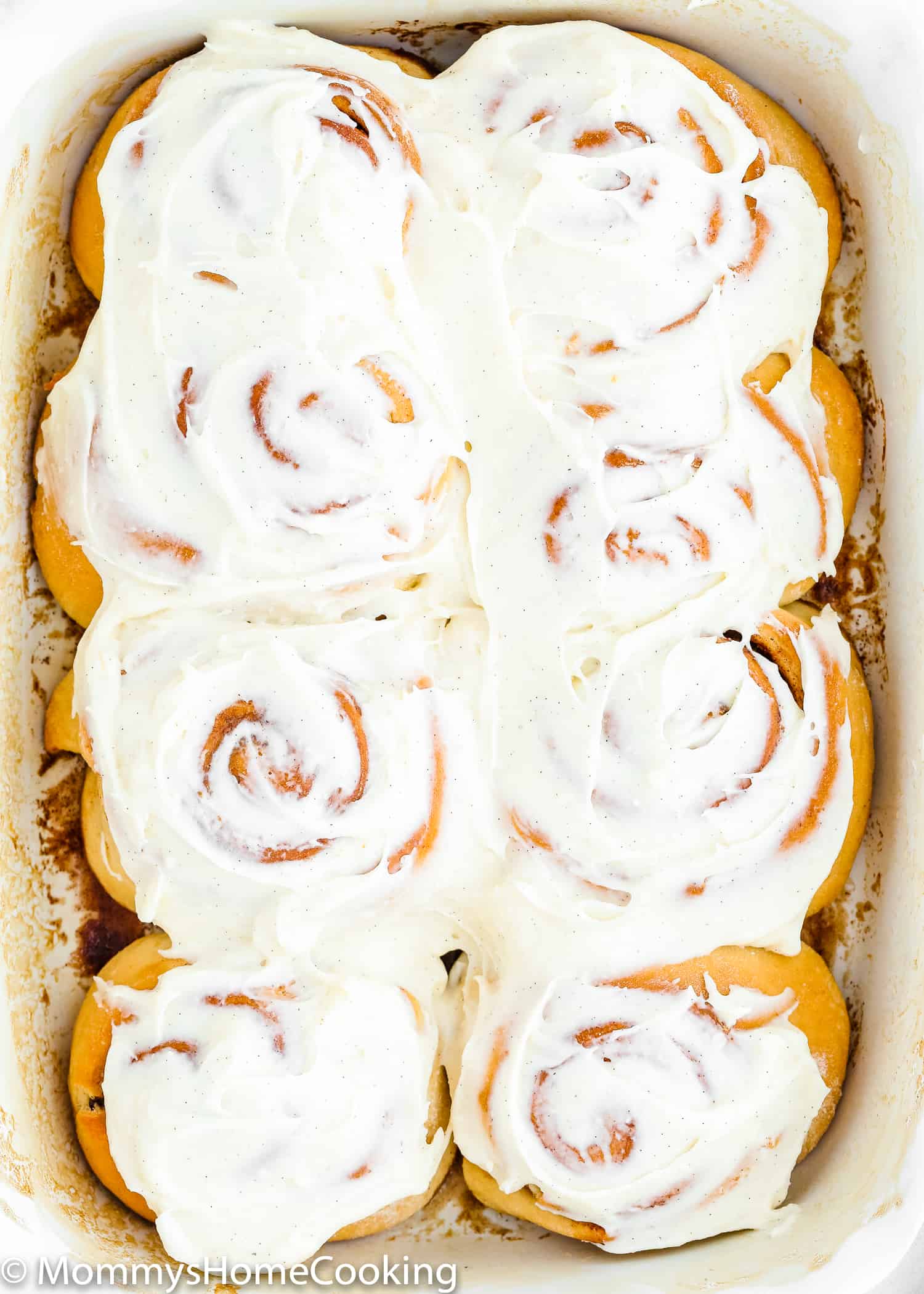 Baked egg-free cinnamon rolls in a baking pan with frosting on top.