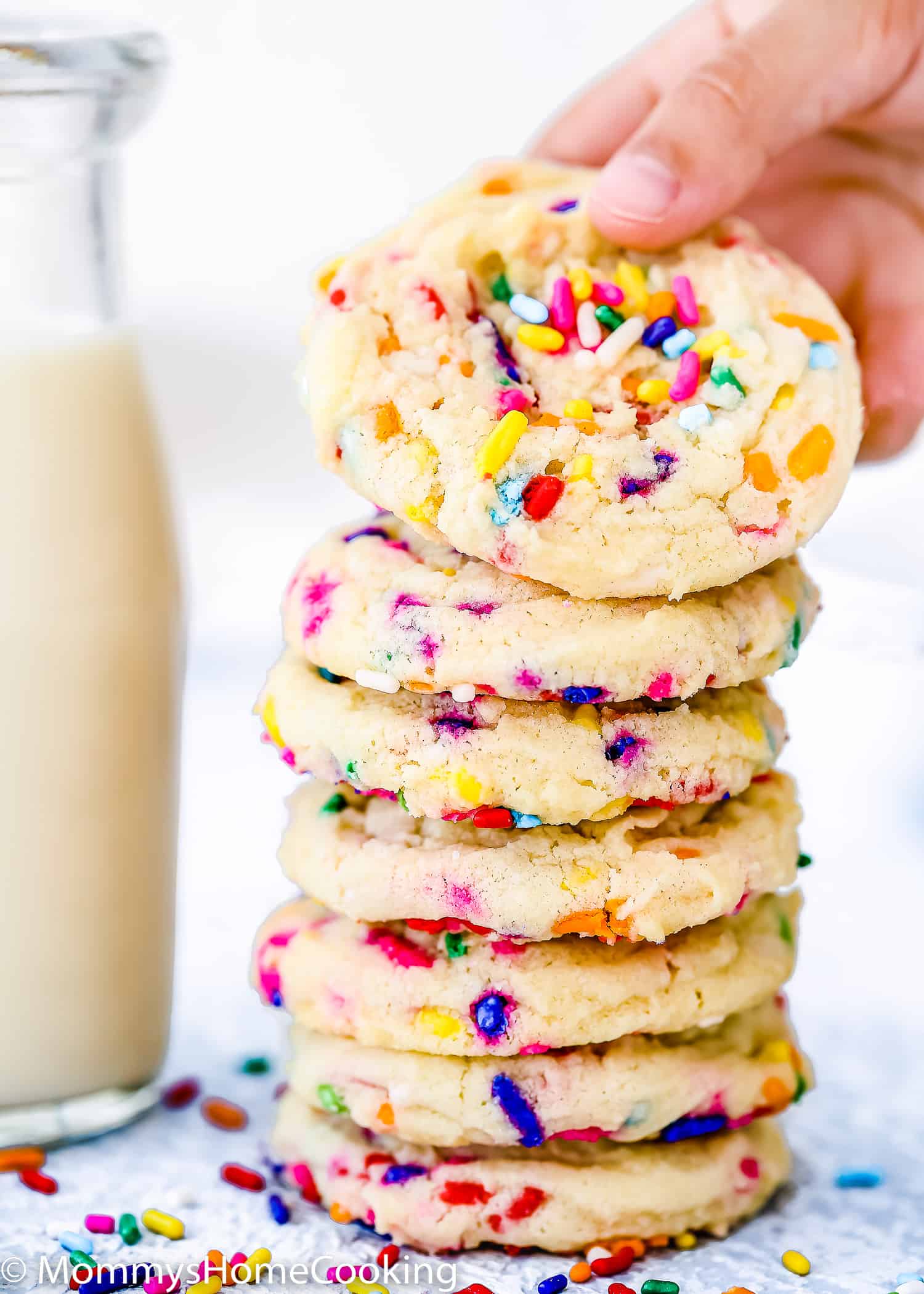 a kid hand taking a egg-free Funfetti cookie from a cookie stack.