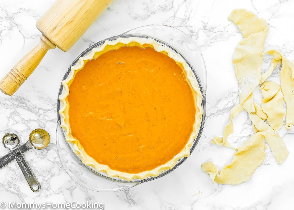 overhead view of a unbaked Eggless Pumpkin Pie with a rolling pin a measuring spoons.