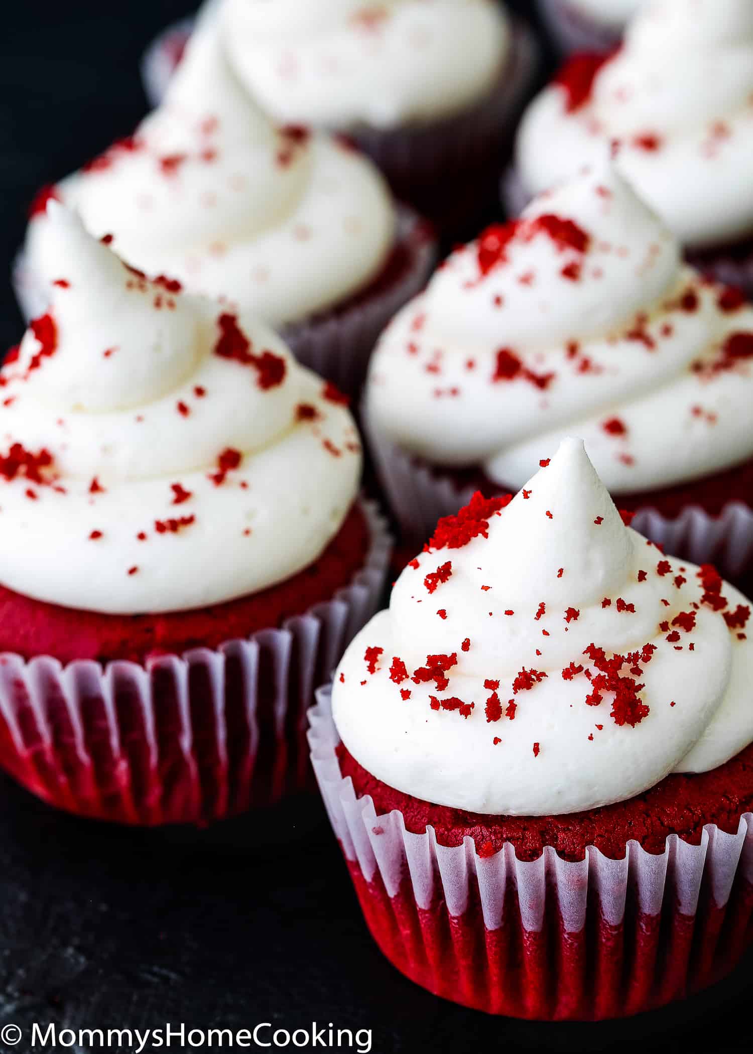 Egg-free red velvet cupcakes with frosting over a black surface.