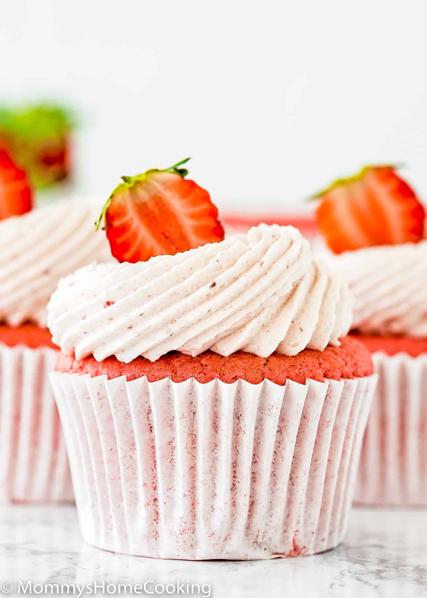 three egg-free Strawberry cupcakes with strawberry buttercream and fresh Strawberry on top.