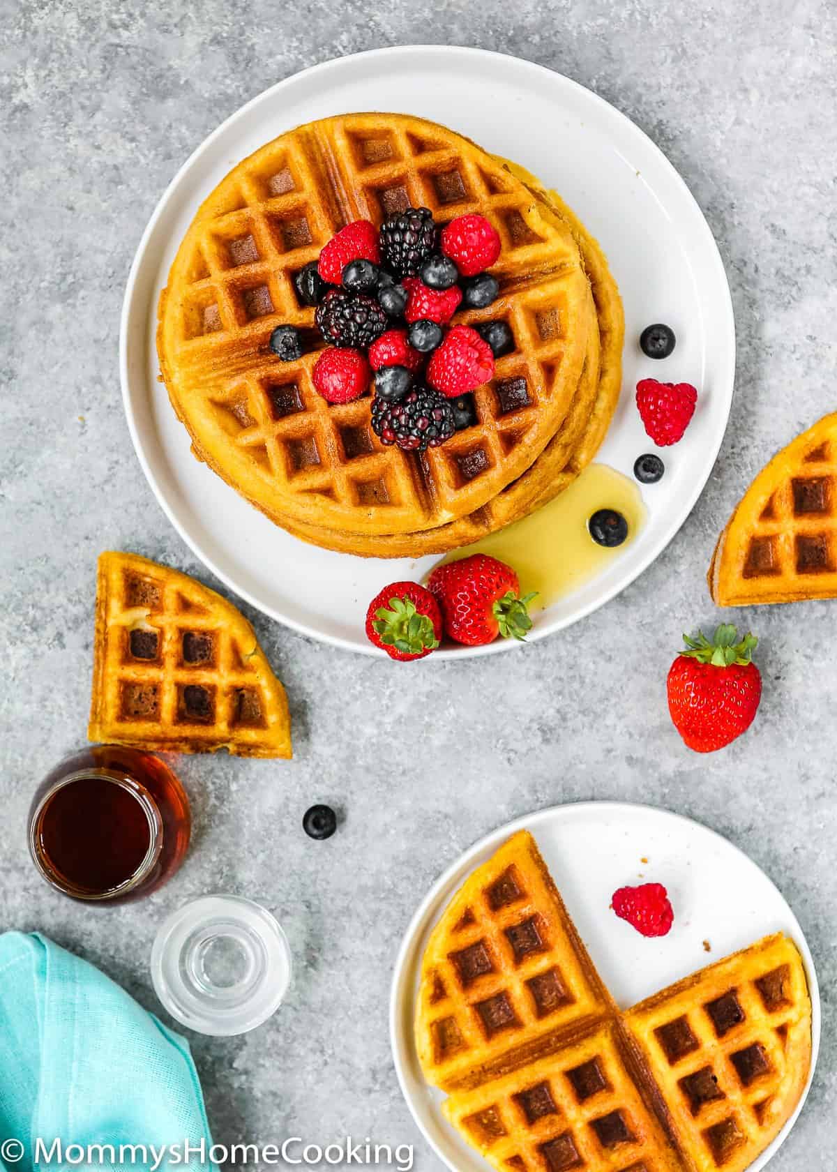 overhead view of eggless waffles on a gray surface with maple syrup and fresh berries.