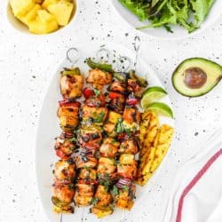 Easy Grilled Hawaiian Chicken Skewers in a white plate with chopped fresh pineapple, green salad and avocado