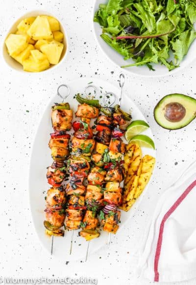 Easy Grilled Hawaiian Chicken Skewers in a white plate with chopped fresh pineapple, green salad and avocado