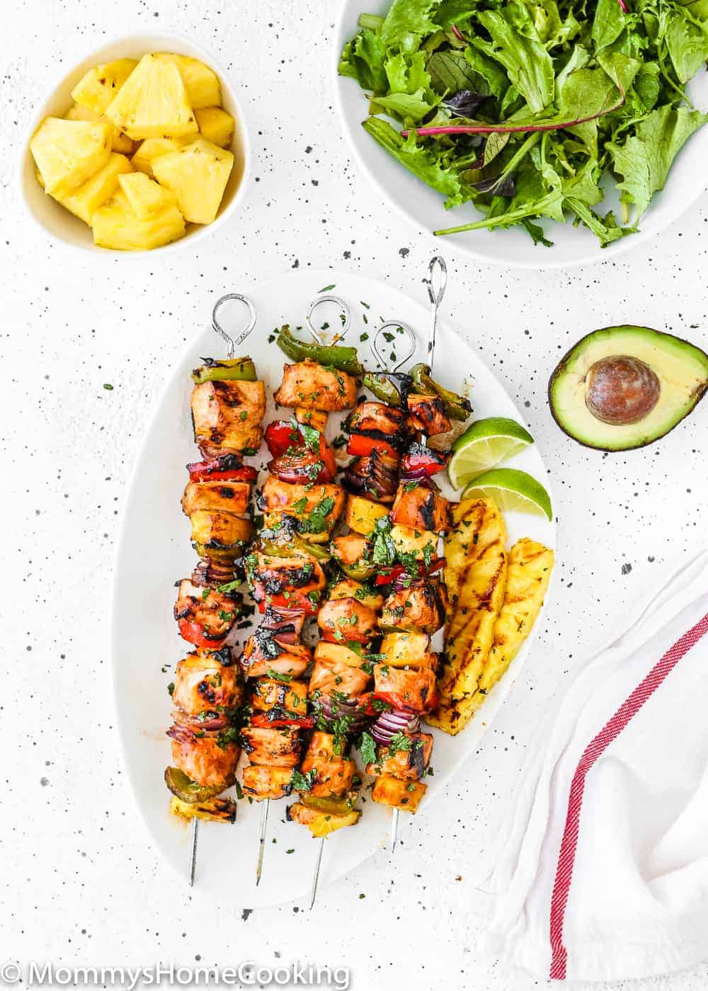 Easy Grilled Hawaiian Chicken Skewers in a white plate with chopped fresh pineapple, green salad and avocado