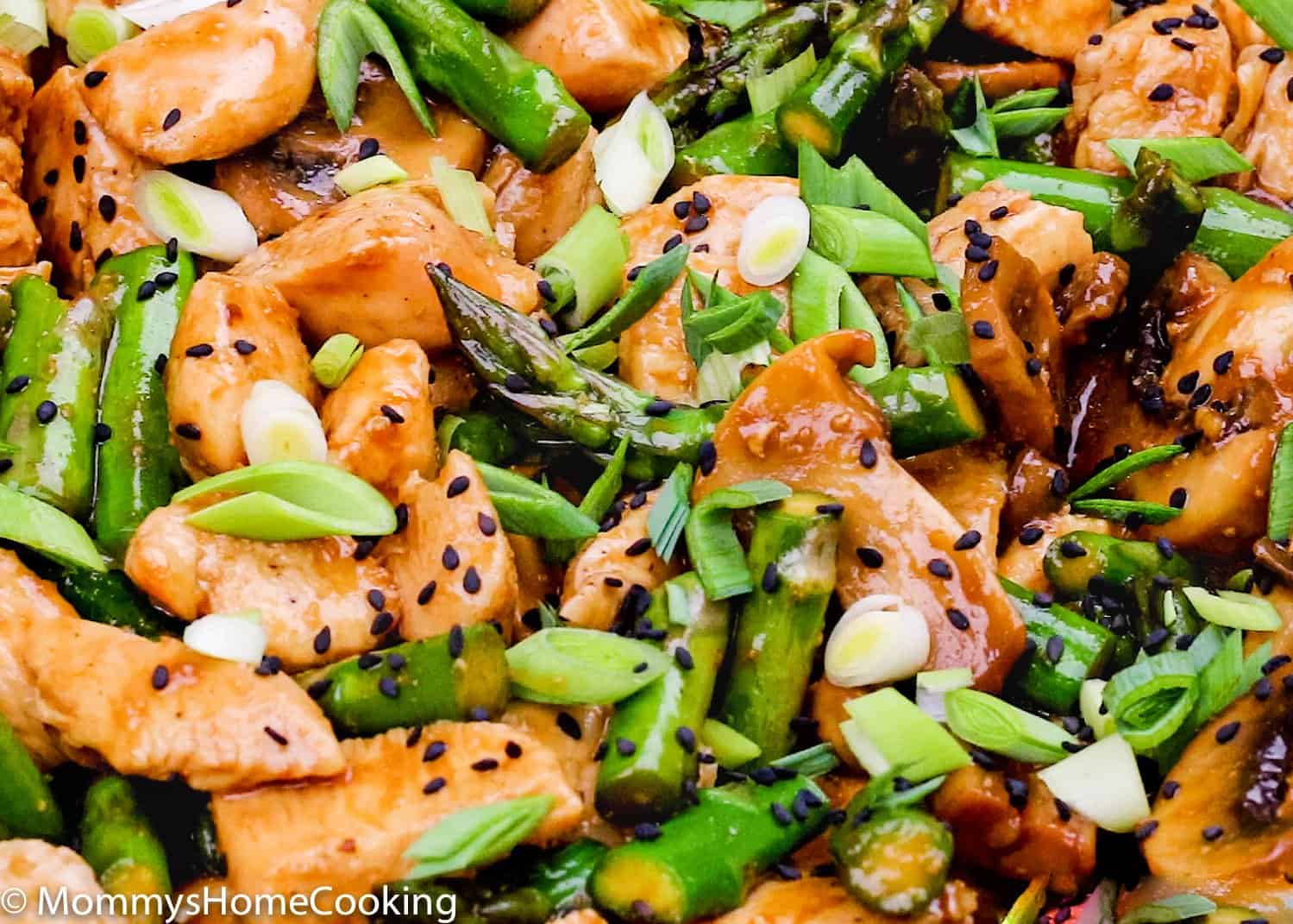 closeup view of chicken, asparagus, mushrooms tossed with sauce and garnished with green onions and sesame seeds. 