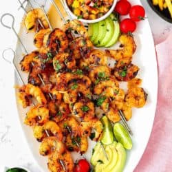 Honey Chipotle Grilled Shrimp in a white oval plate served with sliced avocado, cherry tomatoes and mango salsa