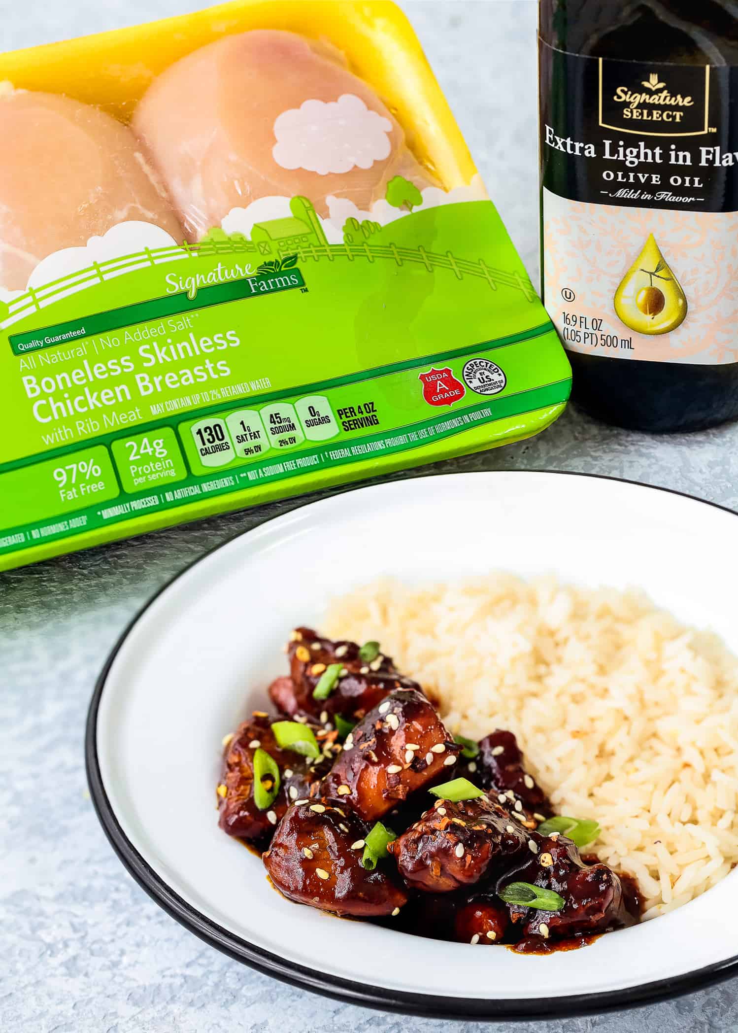 A plate of Instant Pot chicken with a side of rice in front of a package of Signature Farms chicken and Signature Select olive oil.