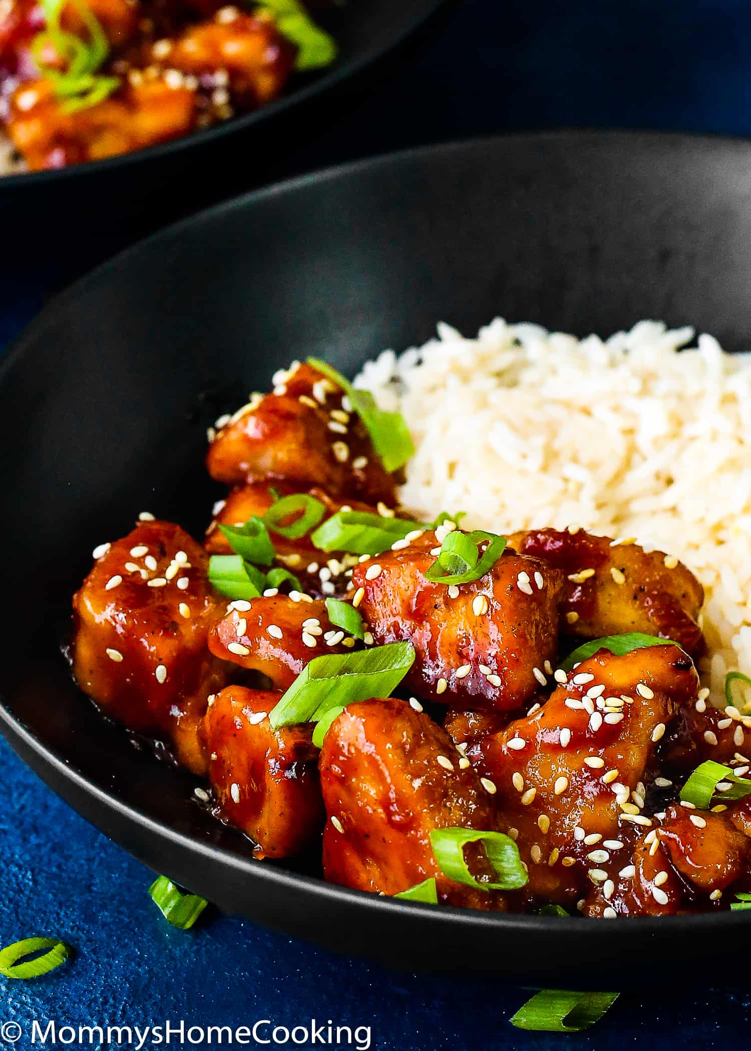 Orange Chicken with sesame seeds and green onion in a black bowl