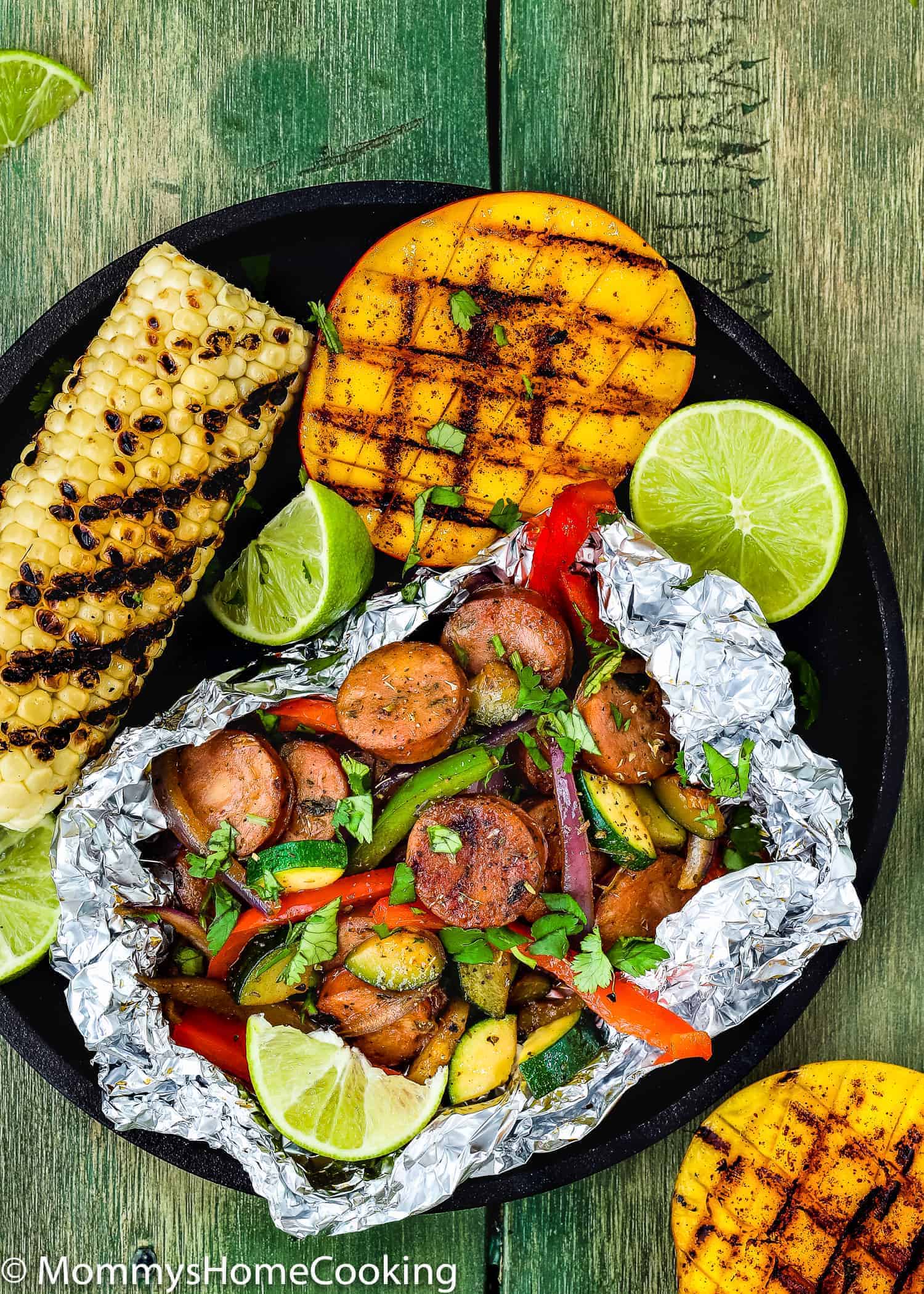 Sausage and Veggies Foil Packets on a plate with grilled mangoes and corn