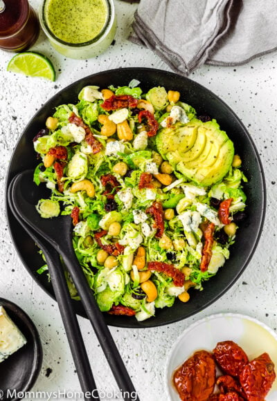 Shaved Brussels Sprout Salad in a salad bowl with serving spoons on the side.