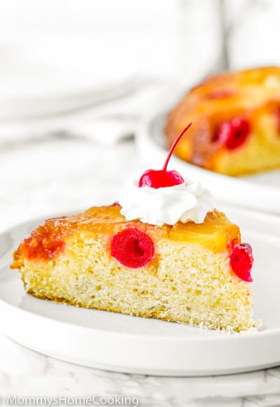 a egg-free pineapple upside-down cake slice on a plate with whipped cream on top and a cherry.