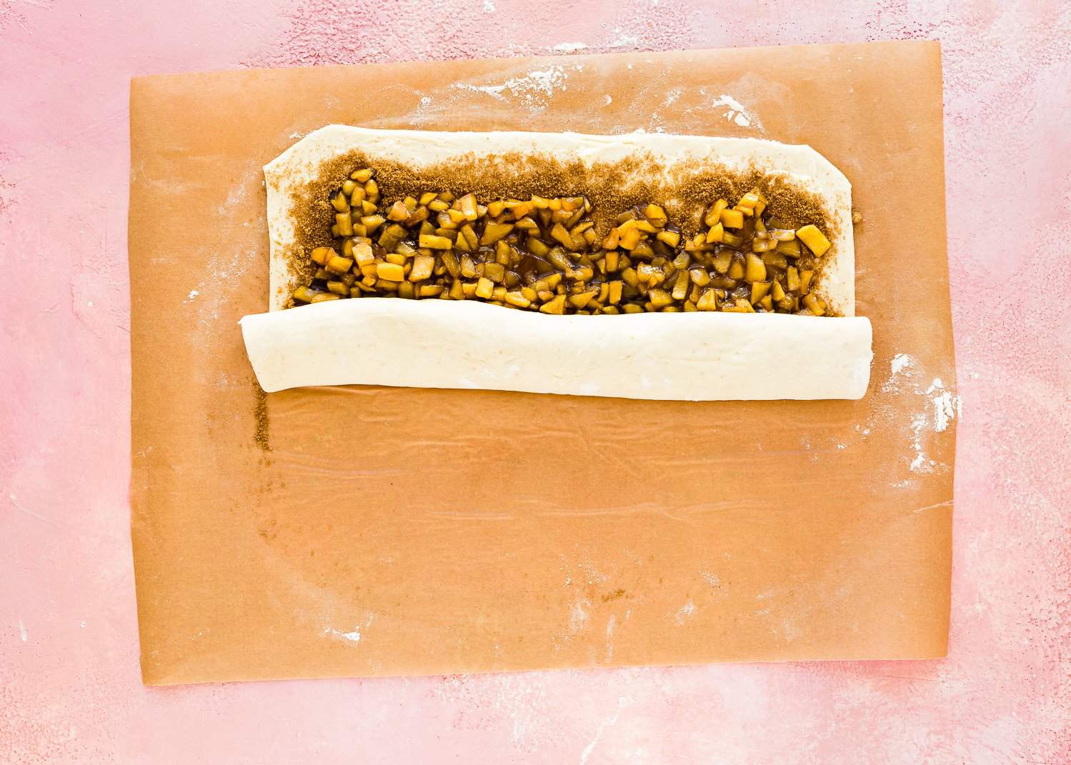 egg-freedough rolled into a rectangle with butter and cinnamon sugar on top over parchment paper being rolled into a log.