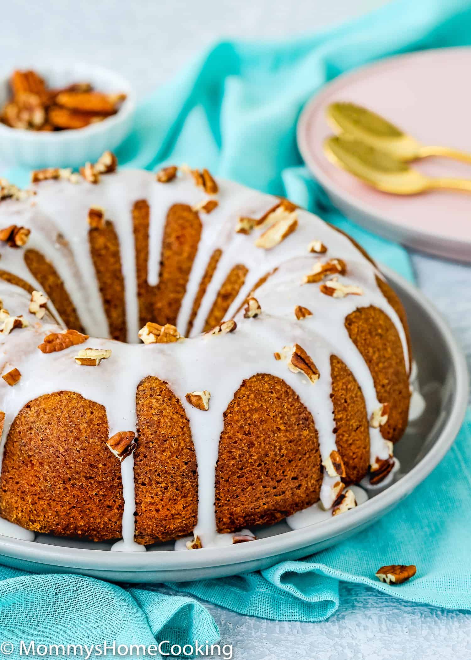 whole eggless carrot cake on a plate with glaze and chopped pecans.