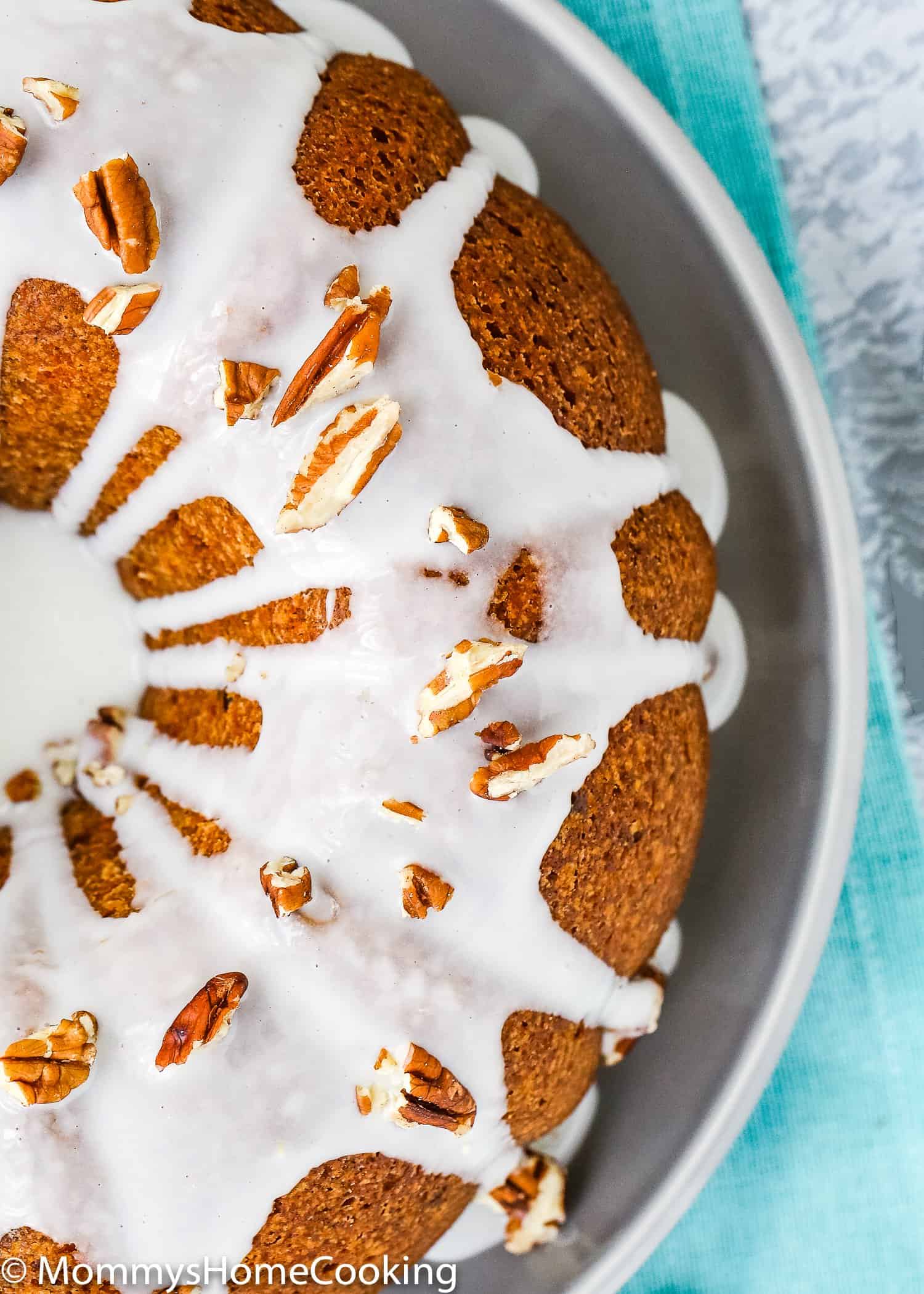 overhead view of an eggless carrot cake on a plate with glaze and chopped pecans