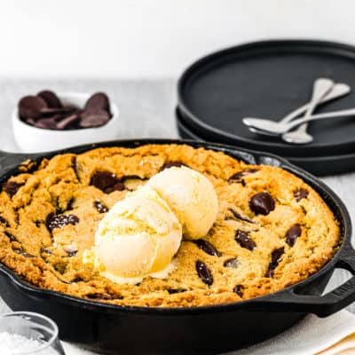 Eggless Chocolate Chip Skillet Cookie with two black plates and dessert spoons in the background..