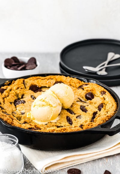 Eggless Chocolate Chip Skillet Cookie with two black plates and dessert spoons in the background..