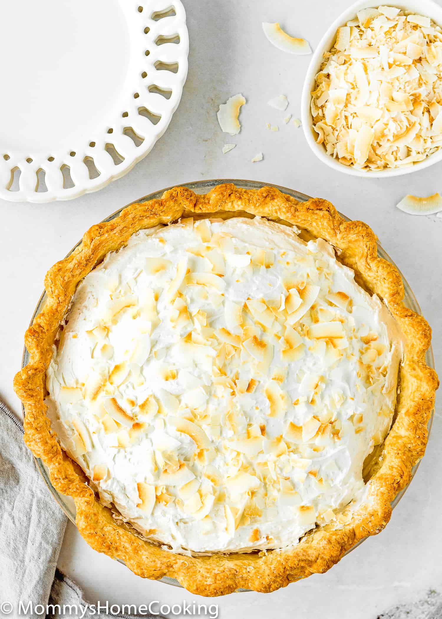 Eggless Coconut Cream Pie whole in a pie dish with two plates on the side and a bowl with toasted coconut flakes. 