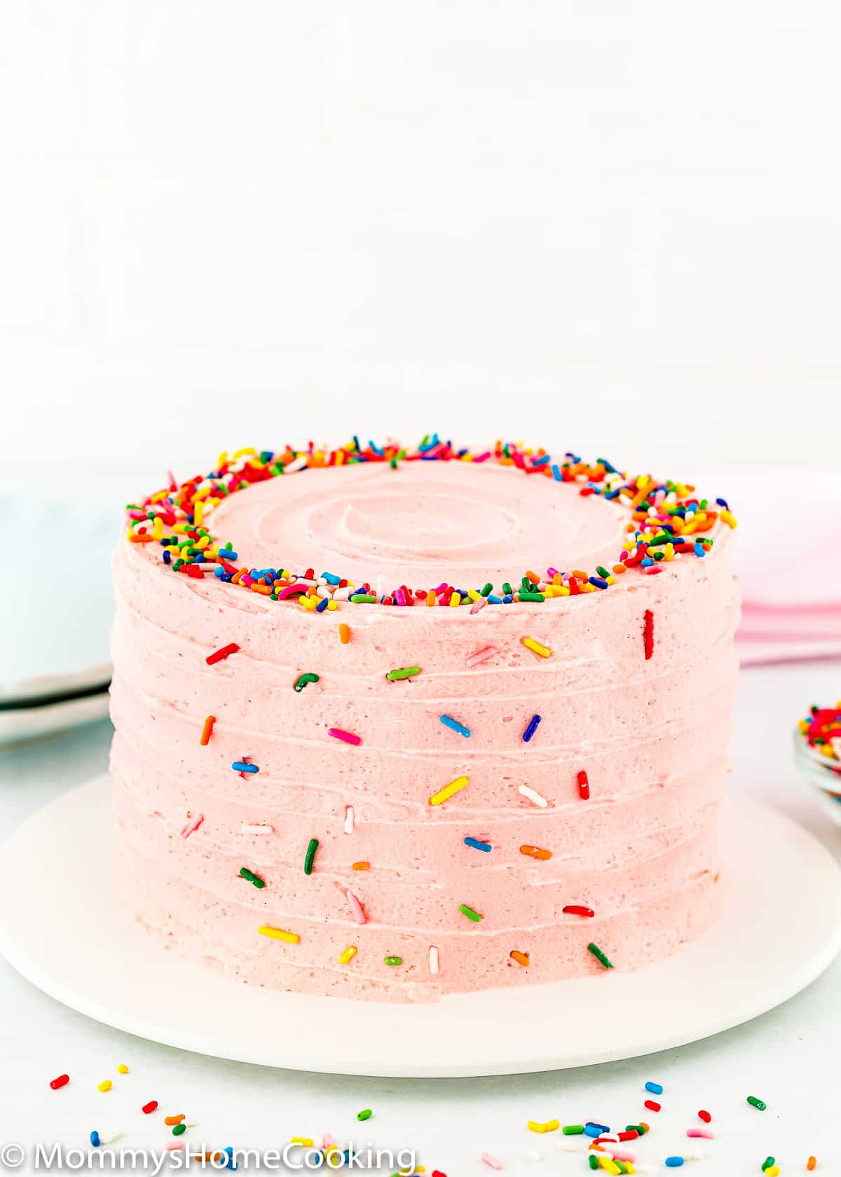 whole egg-free confetti cake with pink buttercream and sprinkles over a cake plate.