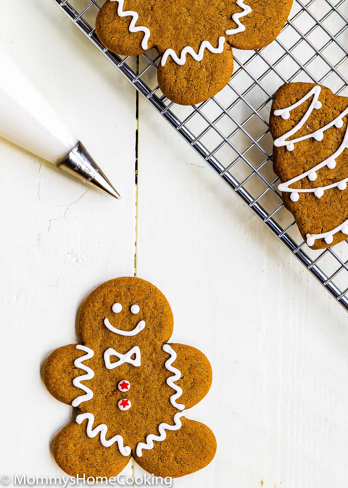 Eggless Gingerbread man Cookie over a wooden surface with a piping bag with eggless royal icing in it.