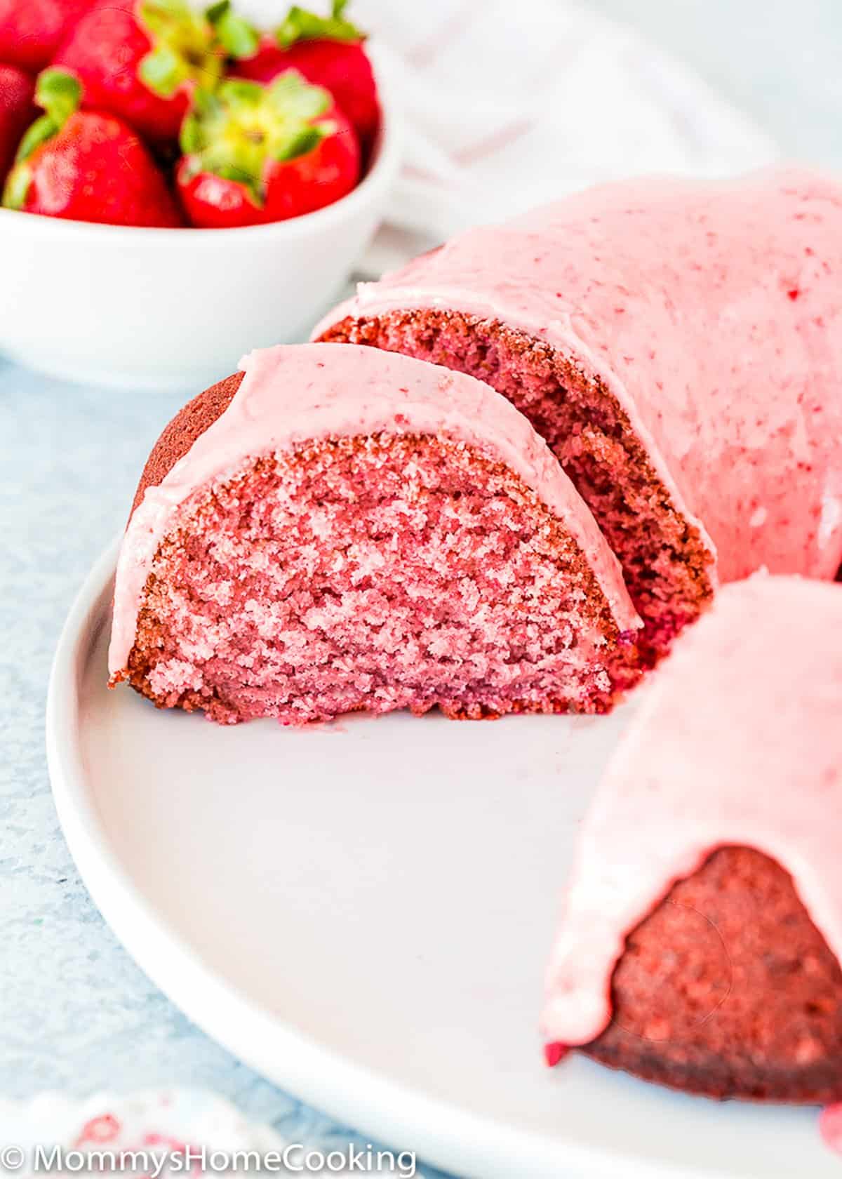 sliced egg-free Strawberry Bundt Cake on a plate with fresh strawberry in the background.