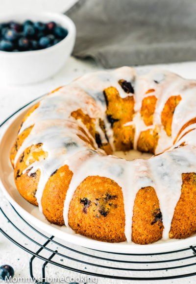 Eggless Lemon Blueberry bundt Cake on a plate with a bowl of blueberries in the backgraound