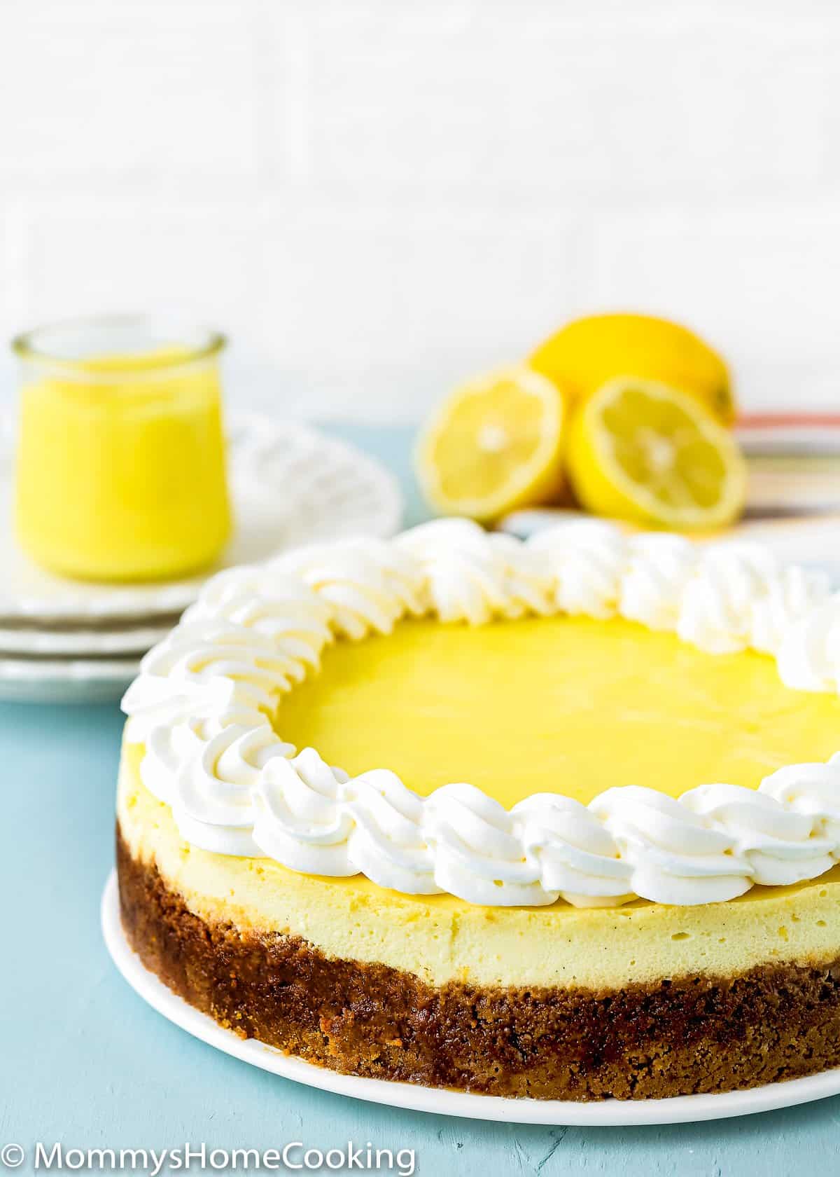 whole eggless lemon cheesecake with eggless lemon crud and whipped cream on a serving plate.