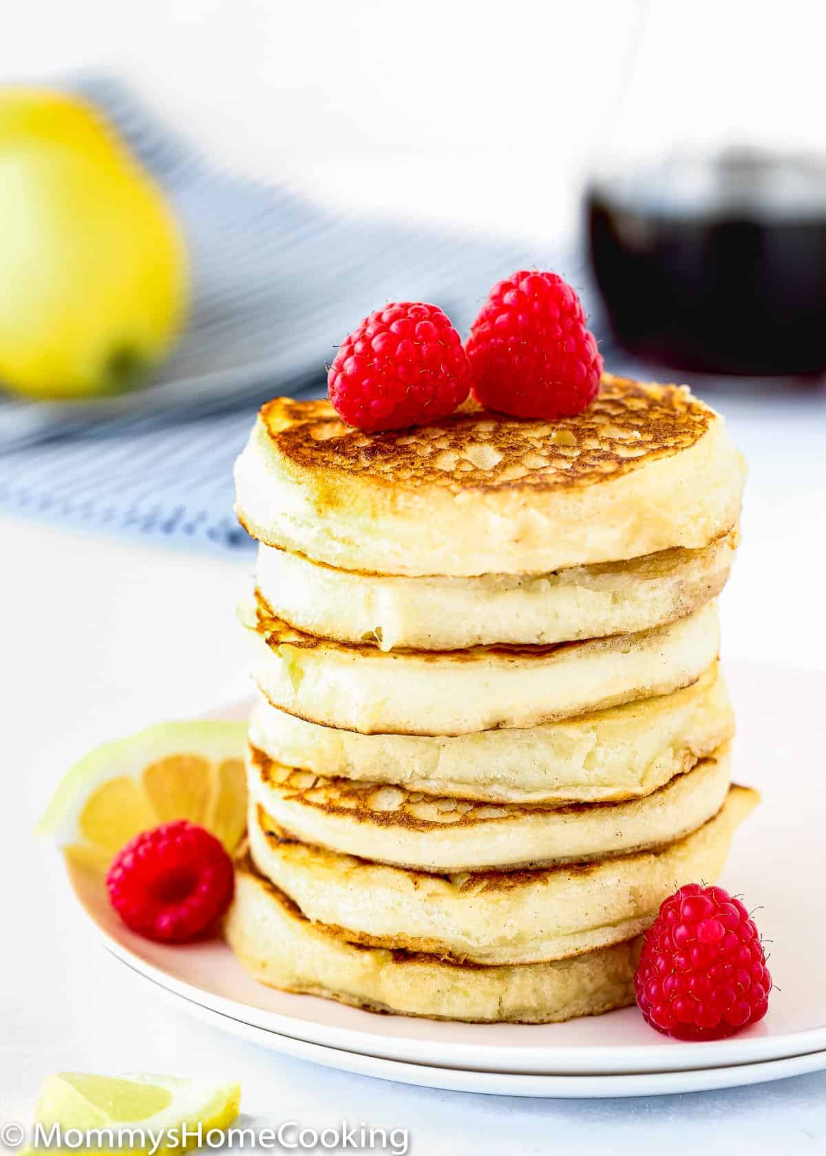 stack of eggless lemon Ricotta pancakes with Raspberries and a lemon slice on a plate.