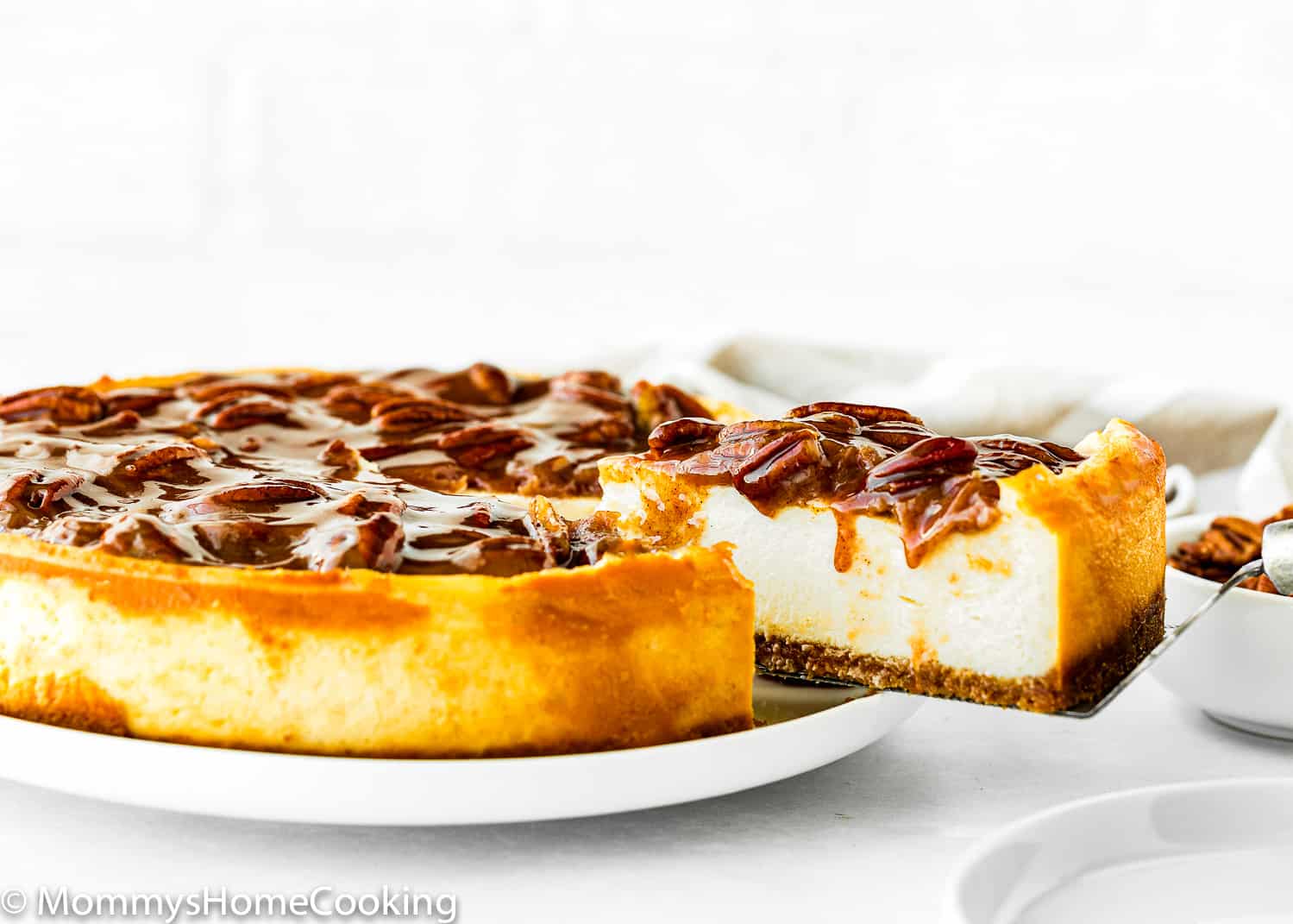 a cake server lifting a slice of Eggless Pecan Pie Cheesecake