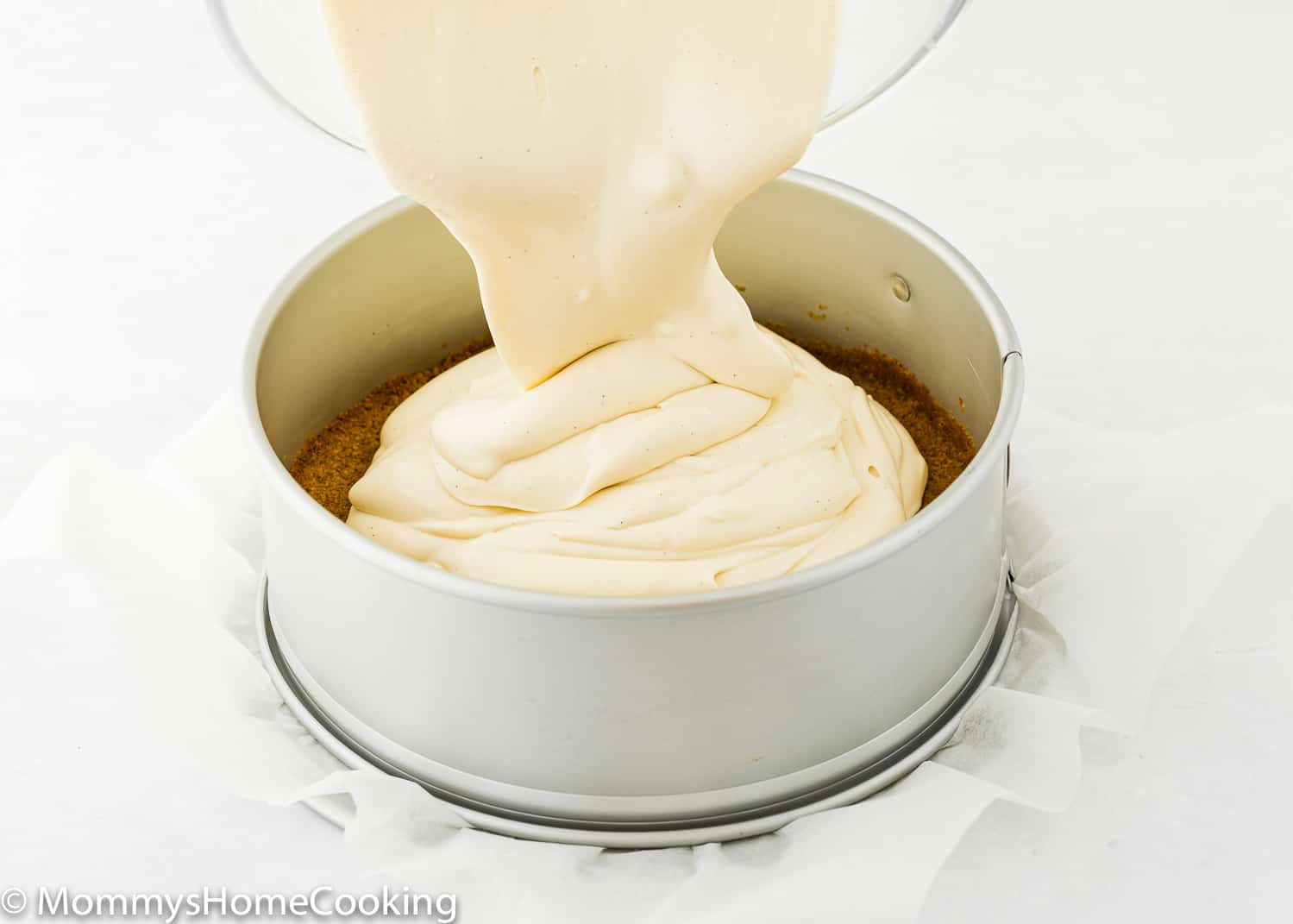 Eggless Cheesecake batter being poured over a graham cracker crust.