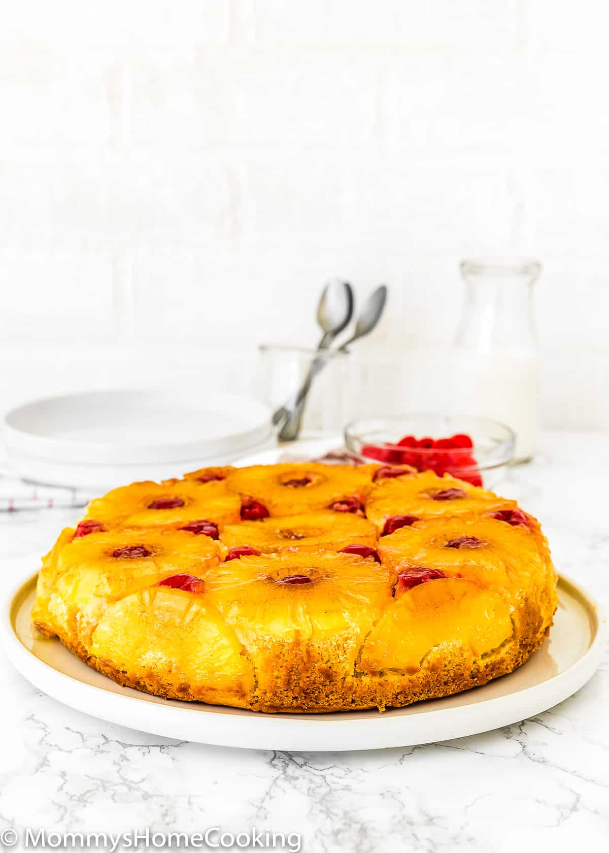 whole Eggless Pineapple Upside Down Cake on a plate over a marble surface.
