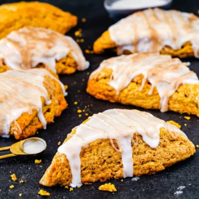 egg-free pumpkin scones with glaze over a black surface.