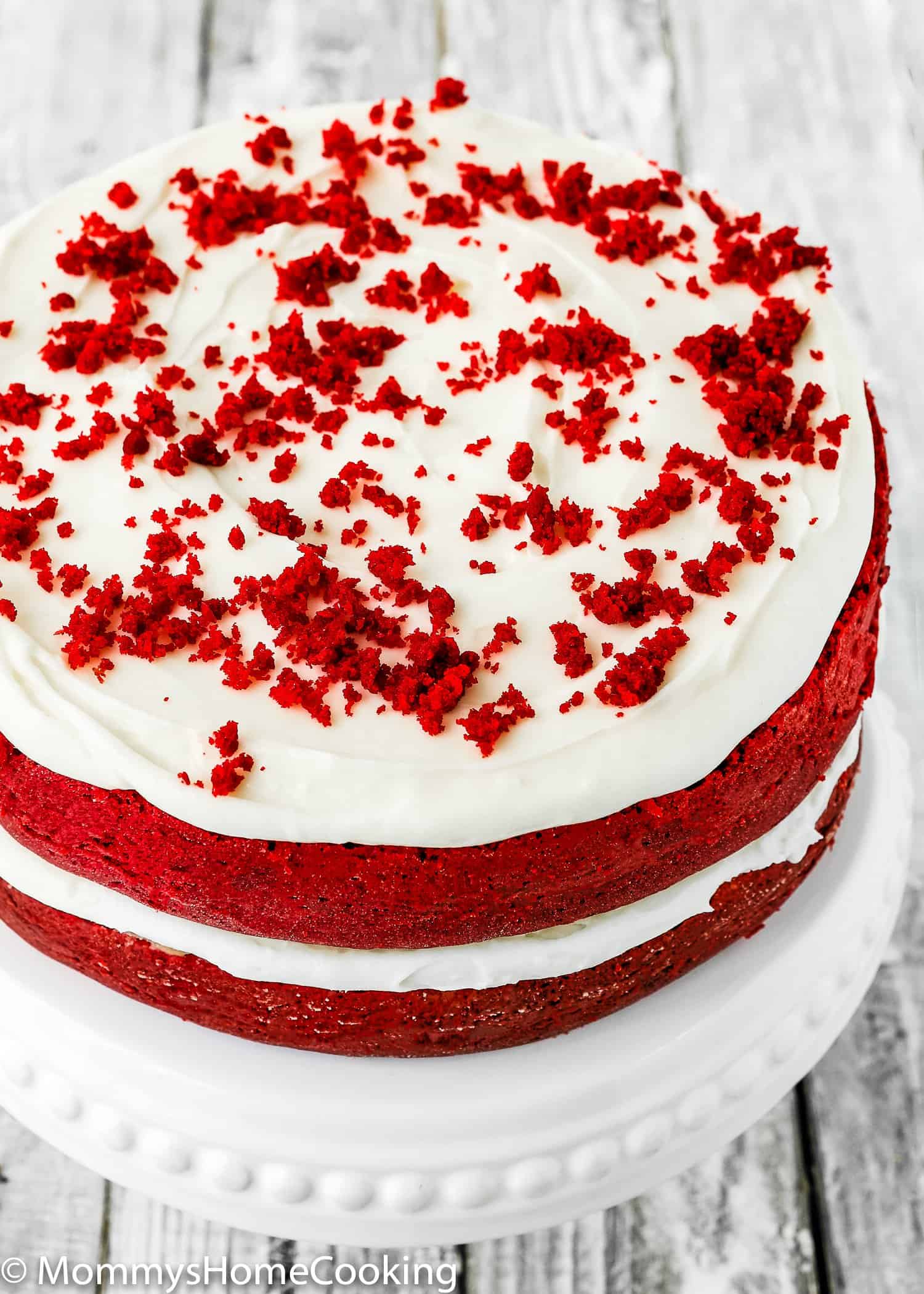 Angled photo of a two tiered red velvet cake with cream cheese frosting, made without eggs.