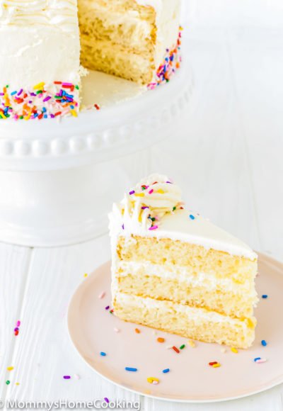 eggless vanilla cake on a cake stand next to plate with a slice of cake