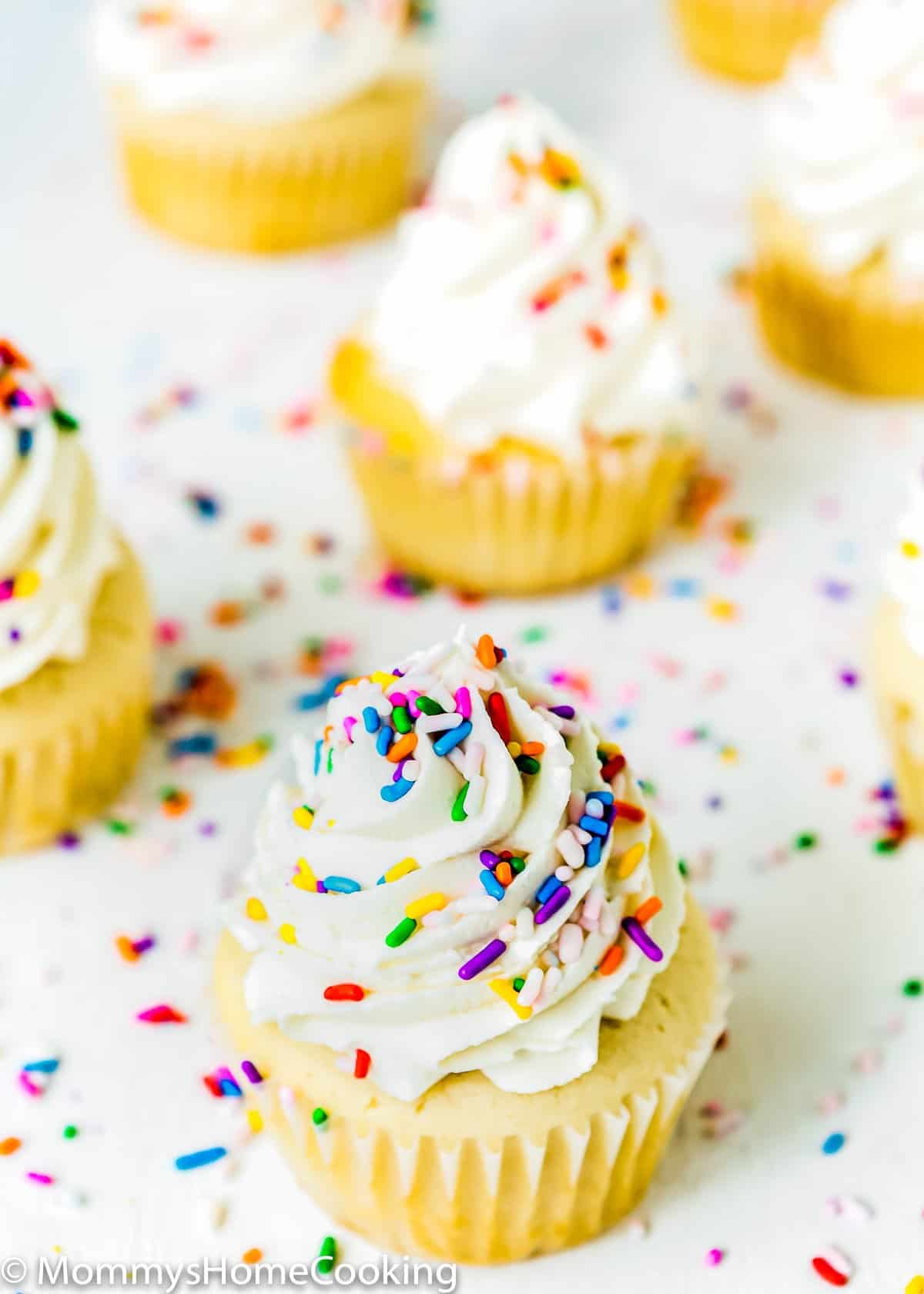 egg-free vanilla cupcakes with frosting and sprinkles over a white surface.