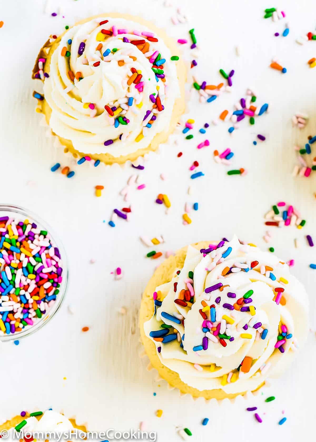 Overhead view of multiple eggless vanilla cupcakes with frosting and sprinkles on top.