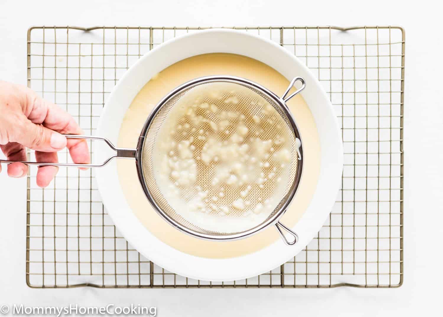 a hand holding a strained showing lumps from a eggless homemade pudding.