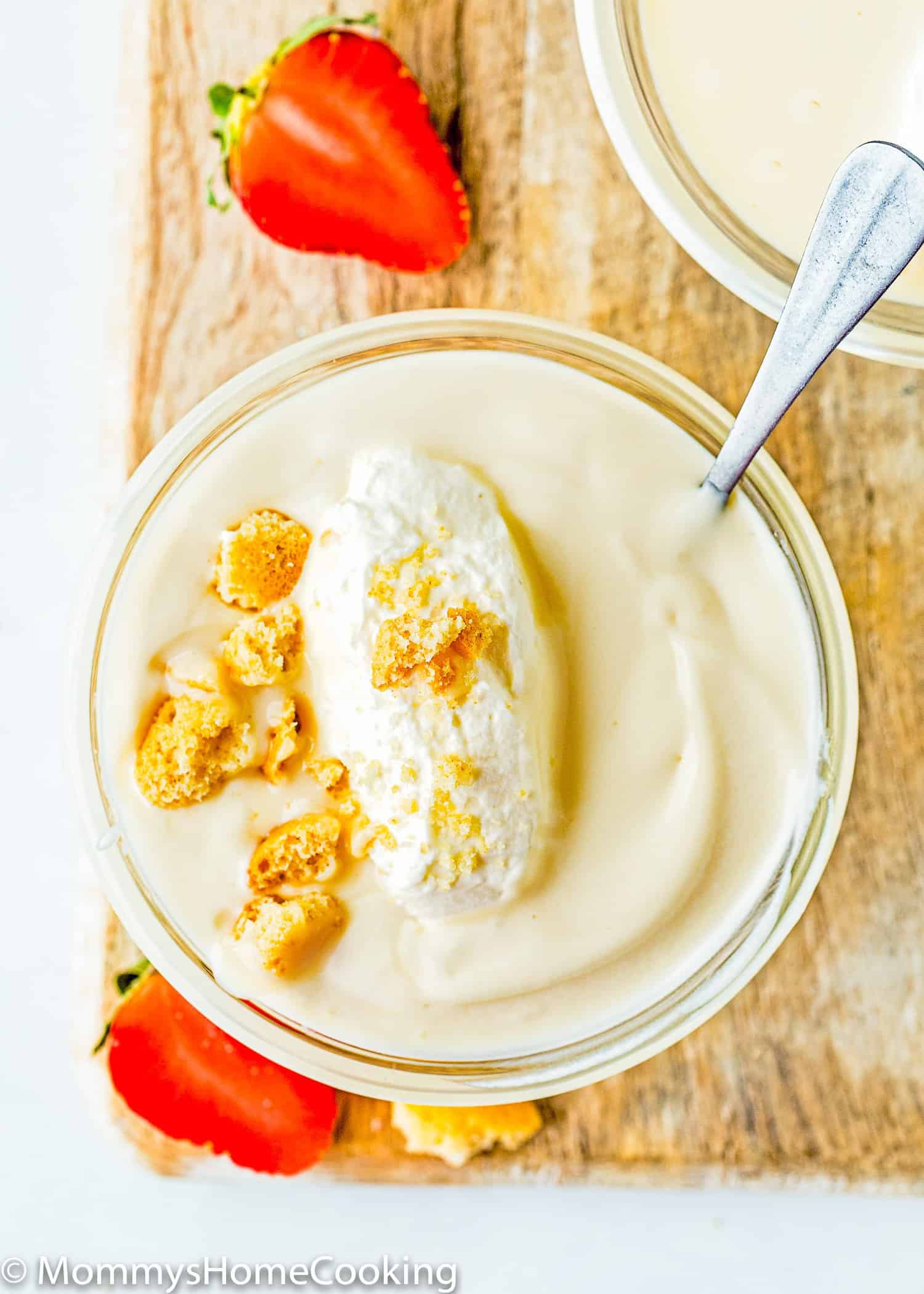 a bowl with Egg free homemade vanilla pudding with whipped cream over a wooden board with fresh strawberries.