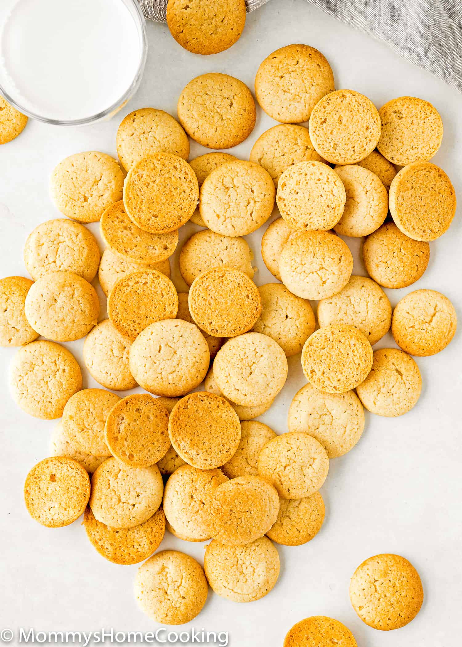 Eggless Vanilla Wafers (Nila Wafers) over a white surface with a glass of milk on the side and a gray kitchen towel.
