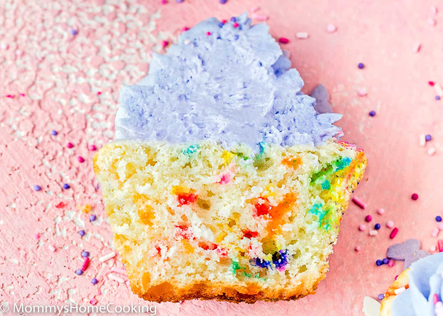 An Eggless Funfetti Cupcake cut in half showing its fluffy texture inside.